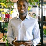 Smiling man holding a tablet in a bright, modern office environment with plants.
